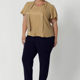 Plus size woman wears semi-fitted design of the Michael Shirt. Tailored yet relaxed feel, this blouse has the right amount of structure without feeling too tight. The V-neckline with delicate neckties adds a touch of feminine elegance, while allowing you to adjust the fit for added comfort and style. The short flutter sleeves, with slits on the shoulders, add a modern, airy feel to the blouse, perfect for this time of year. Available in sizes 8-24.