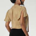 Woven blouse made from luxurious gold soft suede-touch Tencel fabric. This images features a blouse draped beautifully on the body, catching the light in the most flattering way. Though the fabric has no stretch, it offers an effortlessly graceful silhouette that moves with you, creating a striking and sophisticated look. Available in size 8-24.