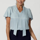 The Michael Shirt in Ice Blue is the perfect blend of modern elegance and workwear chic designed to effortlessly transition from workwear to evening style. This powder blue blouse has flutter sleeves and neck ties that can be tied up with a bow or left undone for a relaxed tuxedo look. Available in size 8-24. 