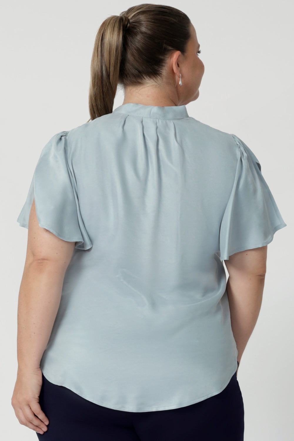 serene Ice Blue, this blouse drapes beautifully on the body, creating a flattering and luminous effect. Though the fabric has no stretch, its elegant drape moves gracefully with you, adding a touch of elevated style to any occasion. The shirttail hemline makes this blouse versatile enough to tuck into high-waisted pants or skirts for a polished office look or leave untucked for a more relaxed vibe.