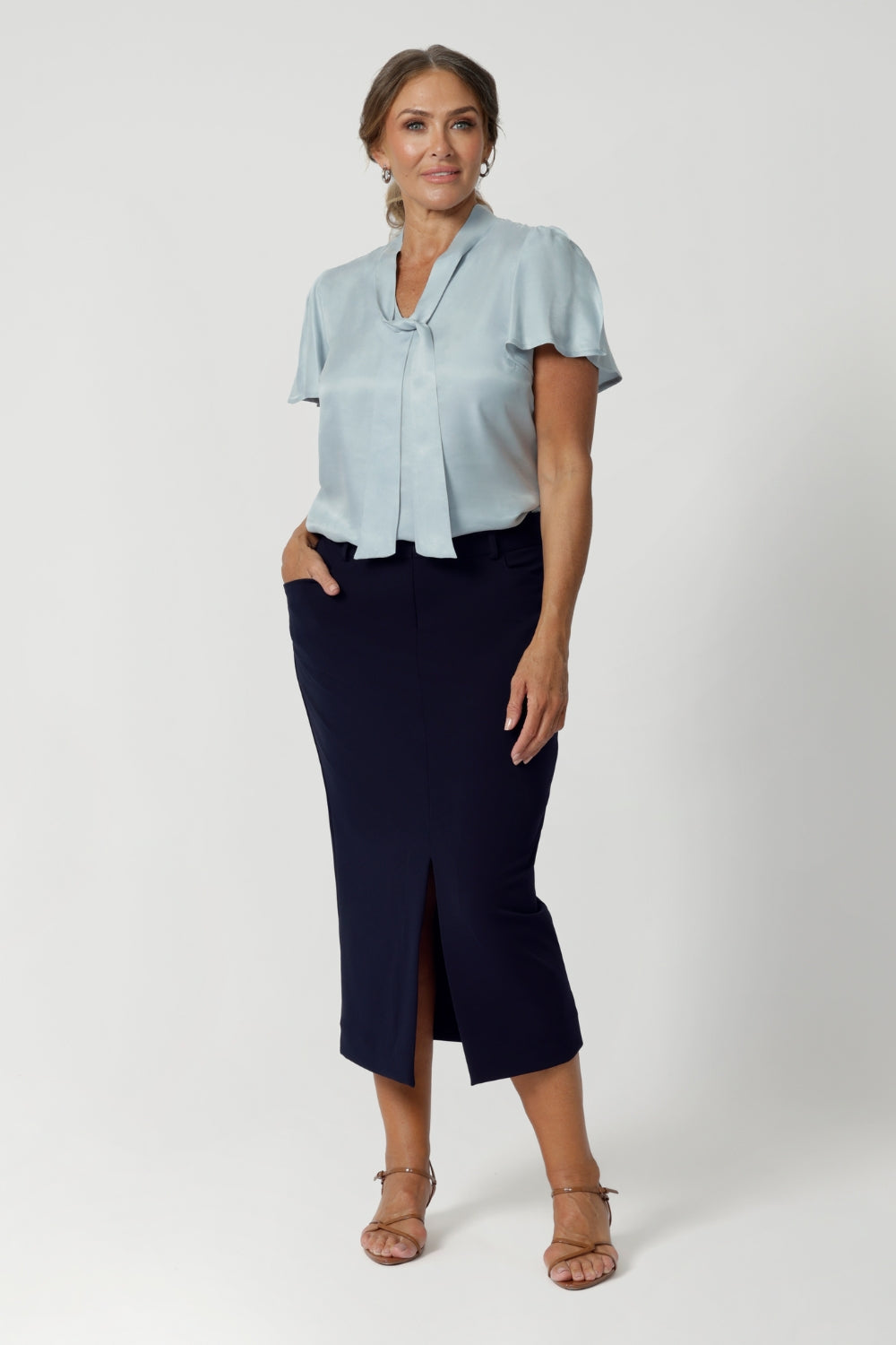 Available in sizes 8-24 and exclusively online at Leina & Fleur, the Michael Shirt in Ice Blue offers endless styling possibilities when paired with other items from our soft suiting collection. Size 12 woman wears blouse with neckties with midi navy skirt and brown kitten heels.  