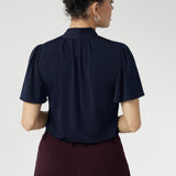 Close up image of Michael top from the back. 40 year old woman wears short sleeved work shirt with neck ties, tucked into work pants. Easy care dry touch jersey fabric used to create cool touch shirt. 