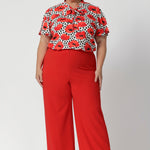 Plus size woman wears poppy printed shirt with tangerine coloured pants, for a vibrant office to evening outfit. Australian-made and available in sizes 8-24, the Michael Shirt offers both style and comfort for the women who wants versatility and elegance in their wardrobe.