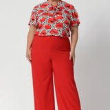 Plus size woman wears poppy printed shirt with tangerine coloured pants, for a vibrant office to evening outfit. Australian-made and available in sizes 8-24, the Michael Shirt offers both style and comfort for the women who wants versatility and elegance in their wardrobe.