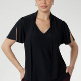 The Michael Top in Black is a timeless wardrobe staple designed for versatile styling. It features a soft tie neckline that can be worn loose, draped, or fastened high for a polished finish, along with short sleeves subtly gathered at the shoulder and finished with a split for elegant movement and coverage.