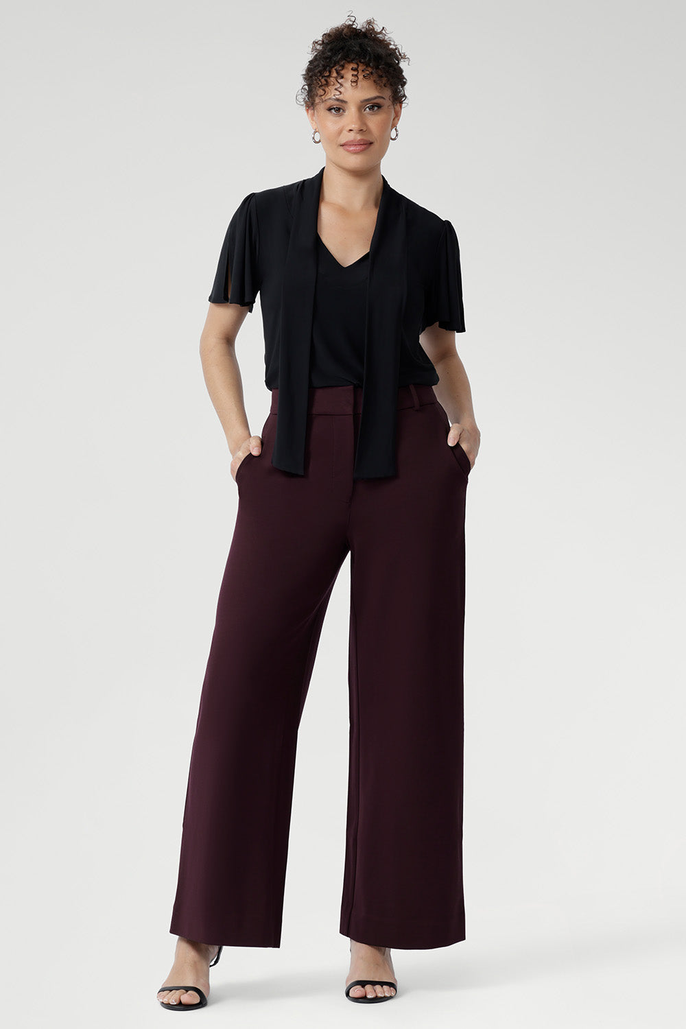 Woman wearing a black top with neck ties and high waisted wide leg pants. Perfect for the office, weekend escapes, or evenings out with friends.