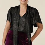 A petite height woman wears a good top for women's evening and event wear. In shimmering bronze foil print, this V-neck top with short flutter sleeves is made in Australia by women's occasionwear brand, Leina and Fleur.