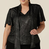A plus size, size 18 woman wears a good top for curvy women's evening and event wear. In shimmering bronze foil print, this V-neck top with short flutter sleeves is Australian-made by women's occasionwear brand, Leina and Fleur.