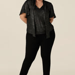 A plus size, size 18 woman wears a good top for curvy women's evening and event wear. In shimmering bronze foil print, this V-neck top with short flutter sleeves is worn with slim leg black trousers for an elegant cocktail wear look.  Made in Australia by women's occasionwear brand, Leina and Fleur.