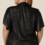 Back view of a plus size, size 18 woman wearing a good top for curvy women's evening and event wear. In shimmering bronze foil print, this V-neck top with short flutter sleeves is made in Australia by women's fashion brand, Leina and Fleur.