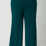 Back view of good workwear pants for plus size women,  Green scuba crepe wide leg pants are worn with a navy jersey top. These wide leg work pants are made in Australia by Australia and New Zealand women's fashion label Leina & Fleur. Available to shop in sizes 8 to 24, this is workwear for plus size to petite height women. 