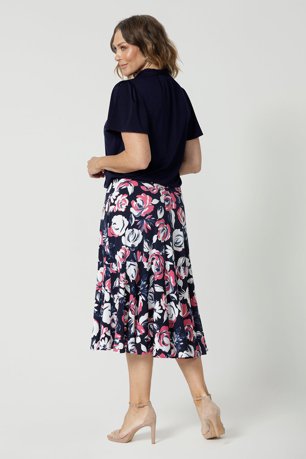 Back view of 40 year old woman wearing a dry touch jersey fabric skirt. 3/4 length skirt made from floral patterned fabric is very colourful with a combination of white and pink roses on navy base. This comfortable work wear skirt is great for both casual wear and dressed up for any occasion. This easy care skirt is made in Australia by Australian and New Zealand women. Leina & Fleur is a woman’s fashion label that stocks sizes from 8 to 24. Shop this comfortable skirt in plus size and petite sizes. 