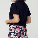 Close up image of Michael top from the back. 40 year old woman wears short sleeved workwear shirt. Made of easy care dry touch fabric paired with Rosie printed skirt for seamless styling option. Leina & Fleur is an Australian brand that created woman's clothing in sizes 8-24, considering petite and plus sizes. 