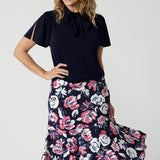 Close up front on image of 40y/o woman wearing a brightly printed midi skirt and navy top. Breathable material used is easy to care dry touch jersey. The floral printed skirt has colours of white, navy and pink. Lightweight skirt is Australian made by women for Australian and New Zealand women. Leina and Fleur is a woman's fashion brand that actively stocks plus and petite sizes ranging from 8 to 24. 