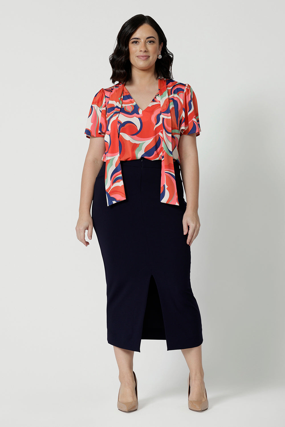 Full body front view of petite woman wearing a midi length work skirt that sits below the calves. This workwear skirt is navy and made of good quality fabric. This comfortable work skirt is stretchy and comfortable. Workwear skirt perfect or an office or corporate environment. 3/4 length skirt is Australian made. Leina & Fleur is a clothing brand for woman that have sizes from 8 to 24. Shop this work skirt in plus sizes and petite sizes. 