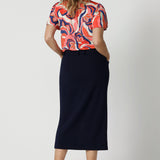 Full body back view of woman wearing midi length skirt. Navy skirt is made to stretch comfortably around the body. Designed with high quality, easy care scube crepe fabric.  Workwear skirt has an above the knee length split. This comfortable work wear skirt was made for any office or corporate setting. Australia made clothing by woman for woman. Made in Australian by Australian and New Zealand women. Leina & Fleur is a woman’s clothing brand that have sizes ranging from 8 to 24. Shop appropriate work skirt.