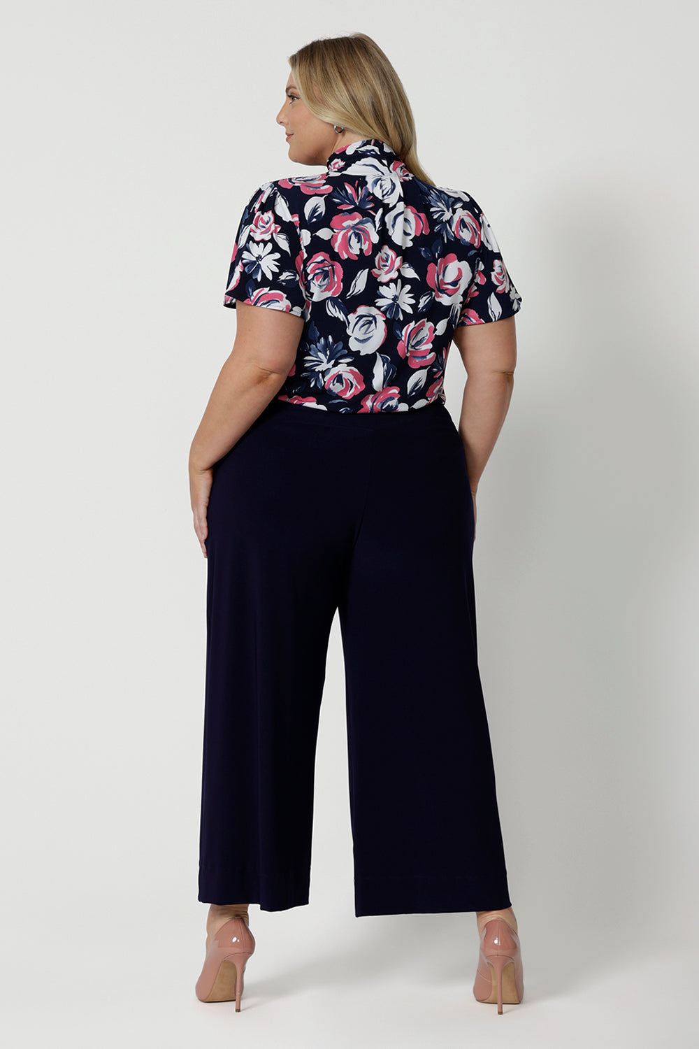 Back view of plus sized model wearing short sleeved shirt. This top is perfect for work due to its easy to care fabric and functioning style. Made of dry touch jersey material. Corporate style blouse was designed in Australia for New Zealand and Australian women. Brand Leina & Fleur is a woman fashions clothing company that proudly stocks sizes 8 to 24.