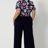 Back view of plus sized model wearing short sleeved shirt. This top is perfect for work due to its easy to care fabric and functioning style. Made of dry touch jersey material. Corporate style blouse was designed in Australia for New Zealand and Australian women. Brand Leina & Fleur is a woman fashions clothing company that proudly stocks sizes 8 to 24.