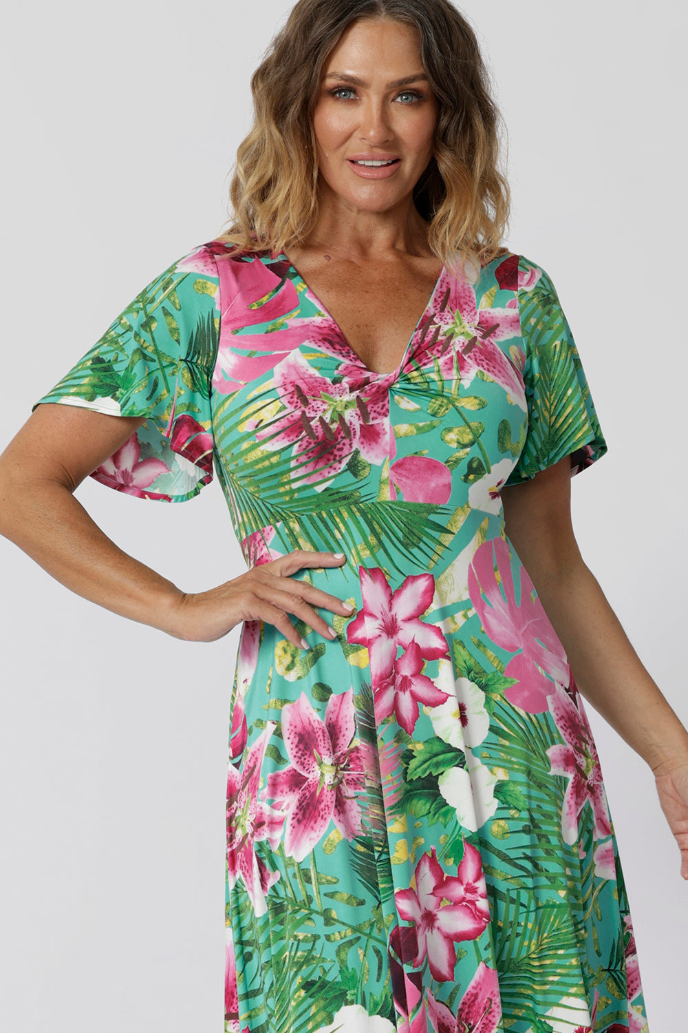 Close up image of floral summer ready dress, featuring a front twist bodice and flutter sleeves. The floral fabric is made of slinky jersey displaying print details in shades of green, pink, white, yellow and brown. The fabric has a soft stretch. The Milly Dress is stocked in 8-24.