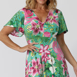 Close up image of floral summer ready dress, featuring a front twist bodice and flutter sleeves. The floral fabric is made of slinky jersey displaying print details in shades of green, pink, white, yellow and brown. The fabric has a soft stretch. The Milly Dress is stocked in 8-24.