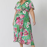 Plus sized woman wears floral dress made with blue slinky jersey fabric with print details in shades of green, pink, white, yellow and brown. Easy care slinky fabric provides a soft stretch and dry, cooling feel. Midi dress is summer event season friendly. Milly Dress in Malibu stocked in sizes 8-24 by fashion brand Leina & Fleur.