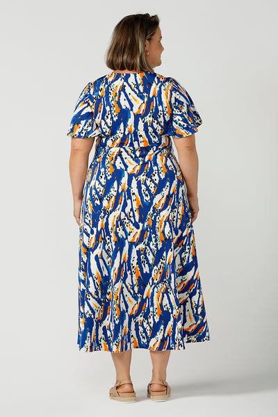Back view of a plus size, size 18 woman wearing a casual slinky jersey midi dress in an abstract print. The dress has short flutter sleeves, a double layer twist front bodice and an asymmetrical skirt - this is a great dress for weekend and travel style.