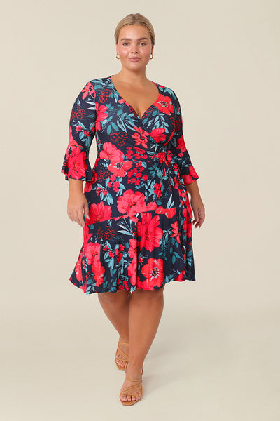 A size 14 petite height woman wears a reversible wrap dress with 3/4 fluted sleeves. Featuring a mini-length skirt with ruffle hem and 3/4 length fluted sleeves, this floral printed jersey dress is has a v-neckline and wears well as an everyday dress. 