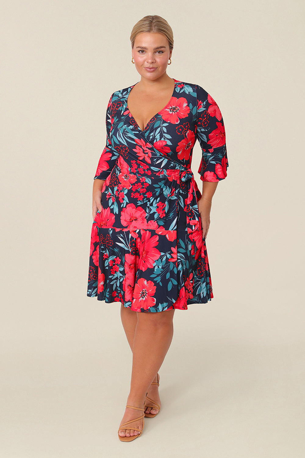 A size 14 petite height woman wears a reversible wrap dress with 3/4 fluted sleeves. Featuring a mini-length skirt with ruffle hem and 3/4 length fluted sleeves, this floral printed jersey dress is has a v-neckline and wears well as an everyday dress. 