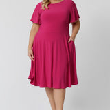 An image of a curve woman wearing a hot pink fit and flare dress made in Australia by Australian womenswear brand Leina & Fleur.