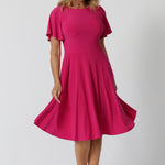 An image of a woman in her forties wearing a hot pink fit and flare dress made in Australia by Australian womenswear brand Leina & Fleur. The dress has a circle skirt and flutter sleeves. 