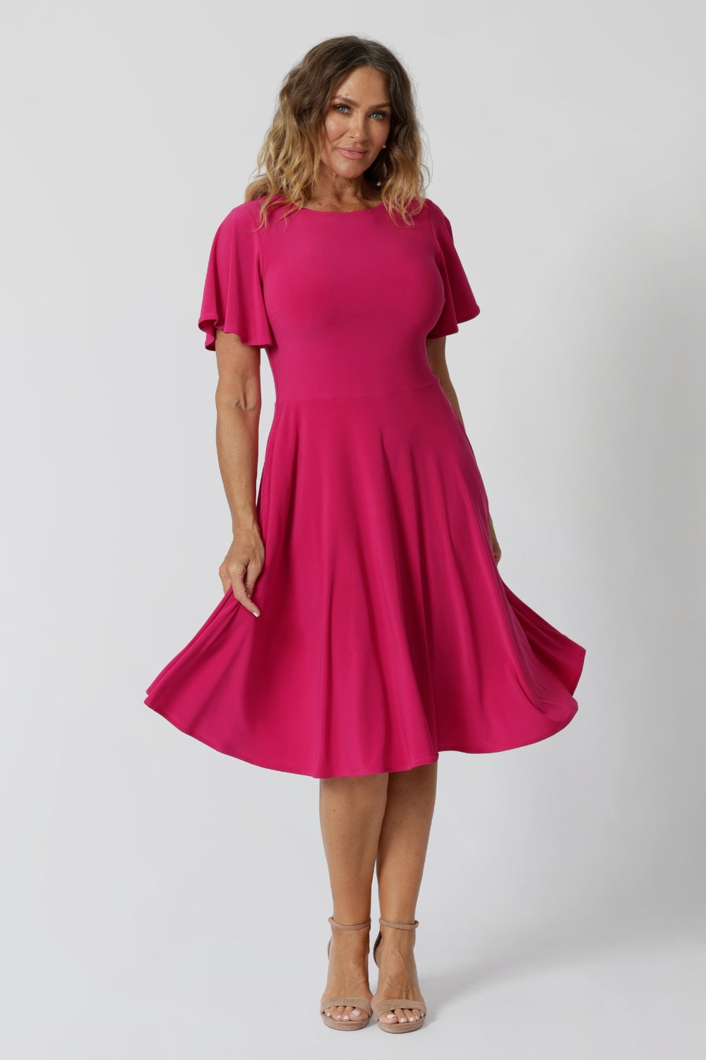 An image of a woman in her forties wearing a hot pink fit and flare dress made in Australia by Australian womenswear brand Leina & Fleur. The dress has a circle skirt and flutter sleeves. 