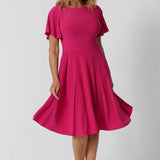 An image of a woman in her forties wearing a hot pink fit and flare dress made in Australia by Australian womenswear brand Leina & Fleur. The dress has a circle skirt and flutter sleeves. 