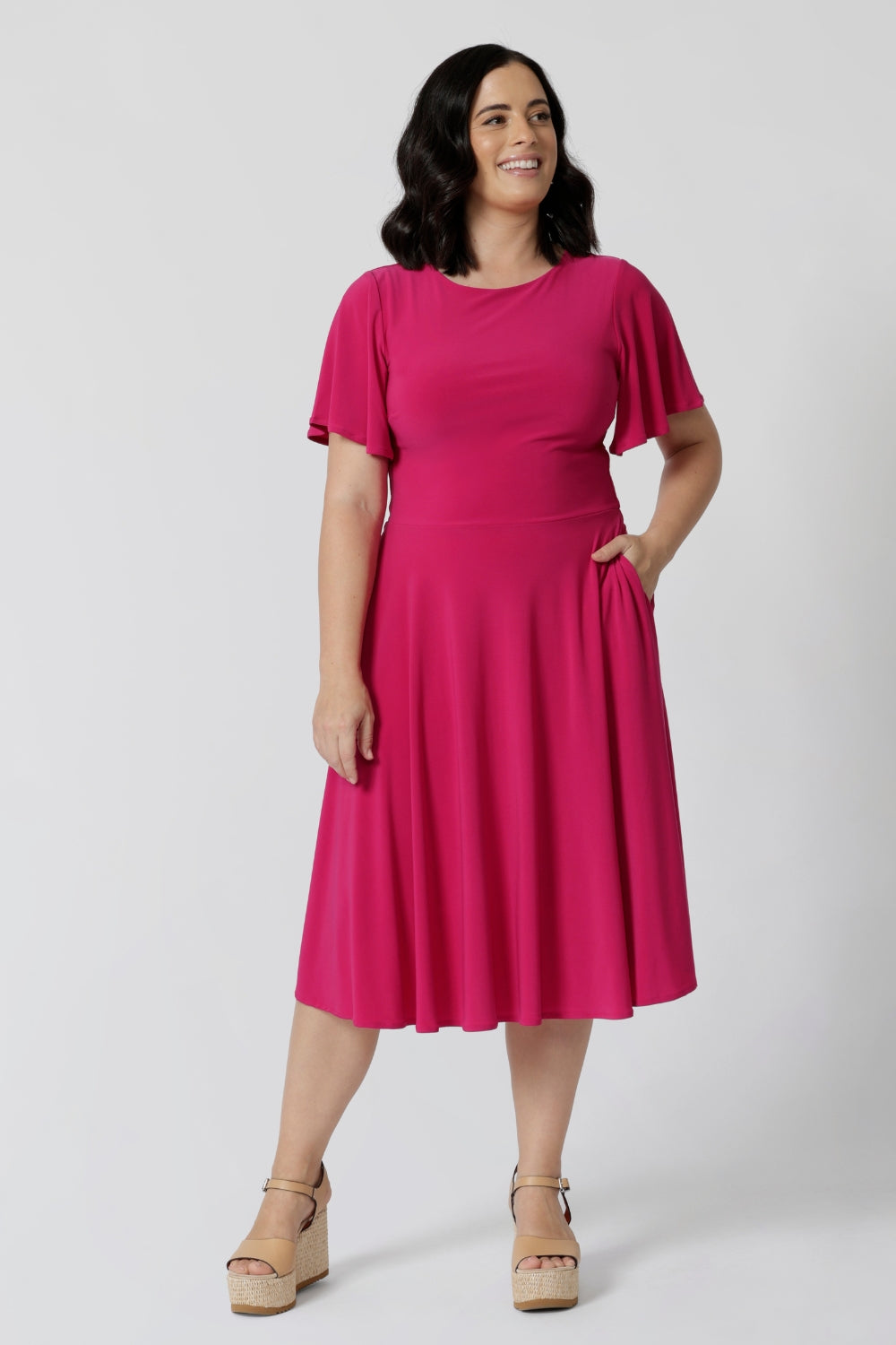 An image of a petite height woman wearing a hot pink fit and flare dress made in Australia by Australian womenswear brand Leina & Fleur.