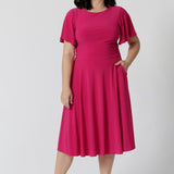 An image of a petite height woman wearing a hot pink fit and flare dress made in Australia by Australian womenswear brand Leina & Fleur.