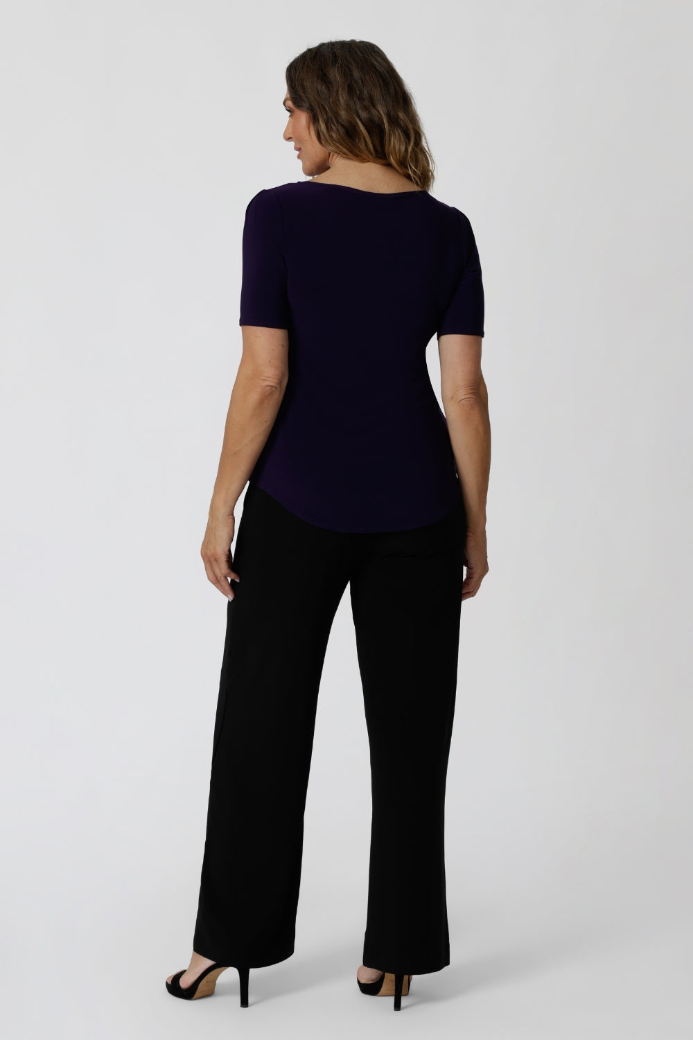 Back view of women's size inclusive work pants. Pictured on a size 12 woman these black comfortable corporate pants are worn with purple jersey top. Full length straight leg pants