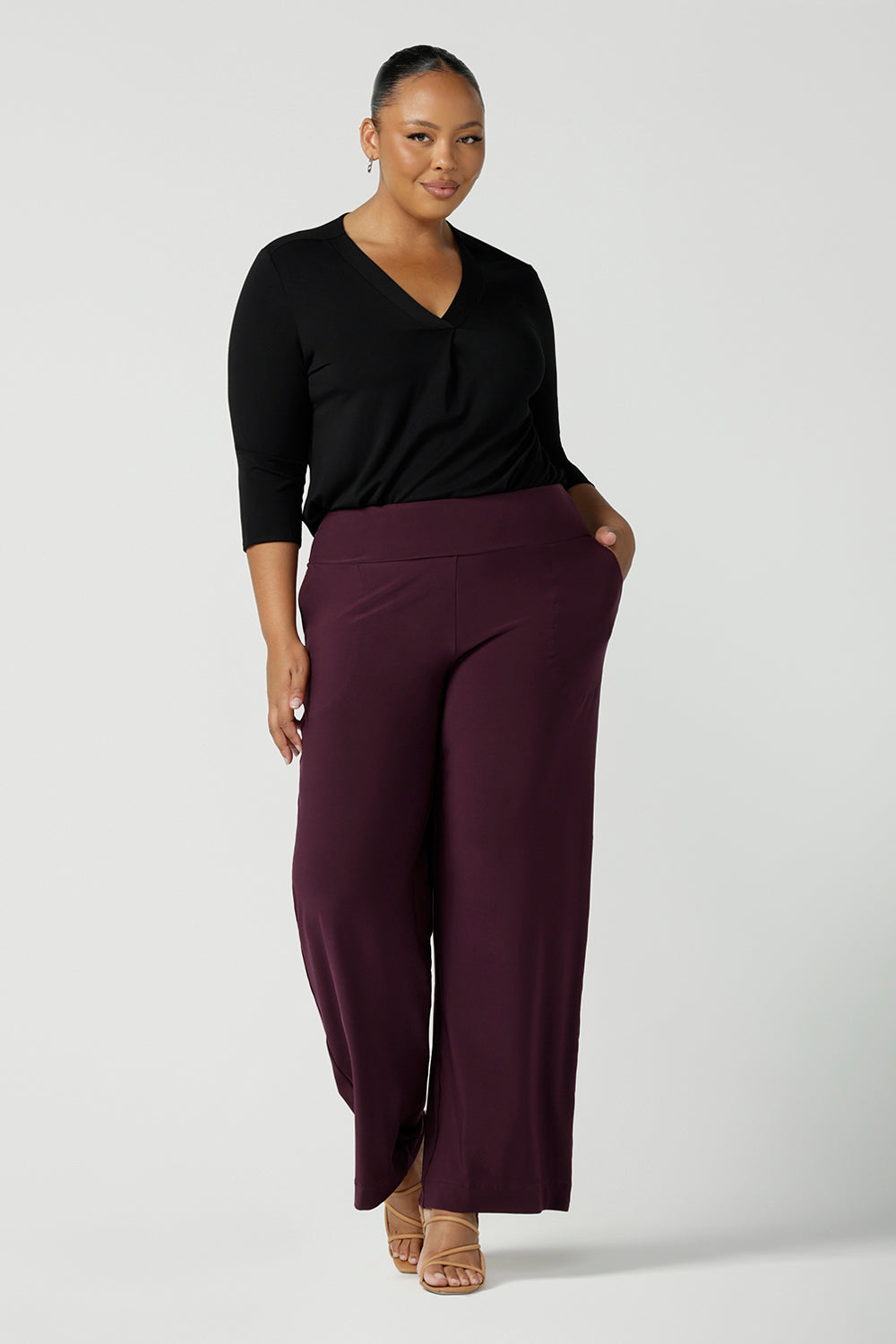 A plus size, size 18 woman wears Mulberry red, straight cut, wide leg, full-length, pull on pants by Australian and New Zealand women's clothing brand, L&F. Featuring a pull-on waistband, these stretch jersey trousers are worn with a a black long sleeve jersey top to create a comfortable outfit for work or casual wear.