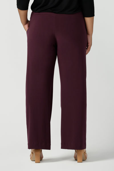 Back view of a plus size, size 18 woman wearing Mulberry red, straight cut, wide leg, full-length, pull on pants by Australian and New Zealand women's clothing brand, L&F. Featuring a pull-on waistband, these stretch jersey trousers are worn with a a black long sleeve jersey top to create a comfortable outfit for work or casual wear.