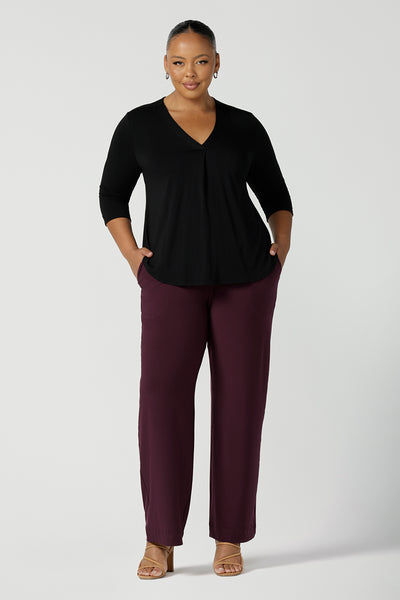 A plus size, size 18 woman wears Mulberry red, straight cut, wide leg, full-length, pull on pants by Australian and New Zealand women's fashion brand, Leina & Fleur. Featuring a pull-on waistband, these stretch jersey trousers are worn with a black long sleeve jersey top to create a comfortable outfit for work or casual wear.