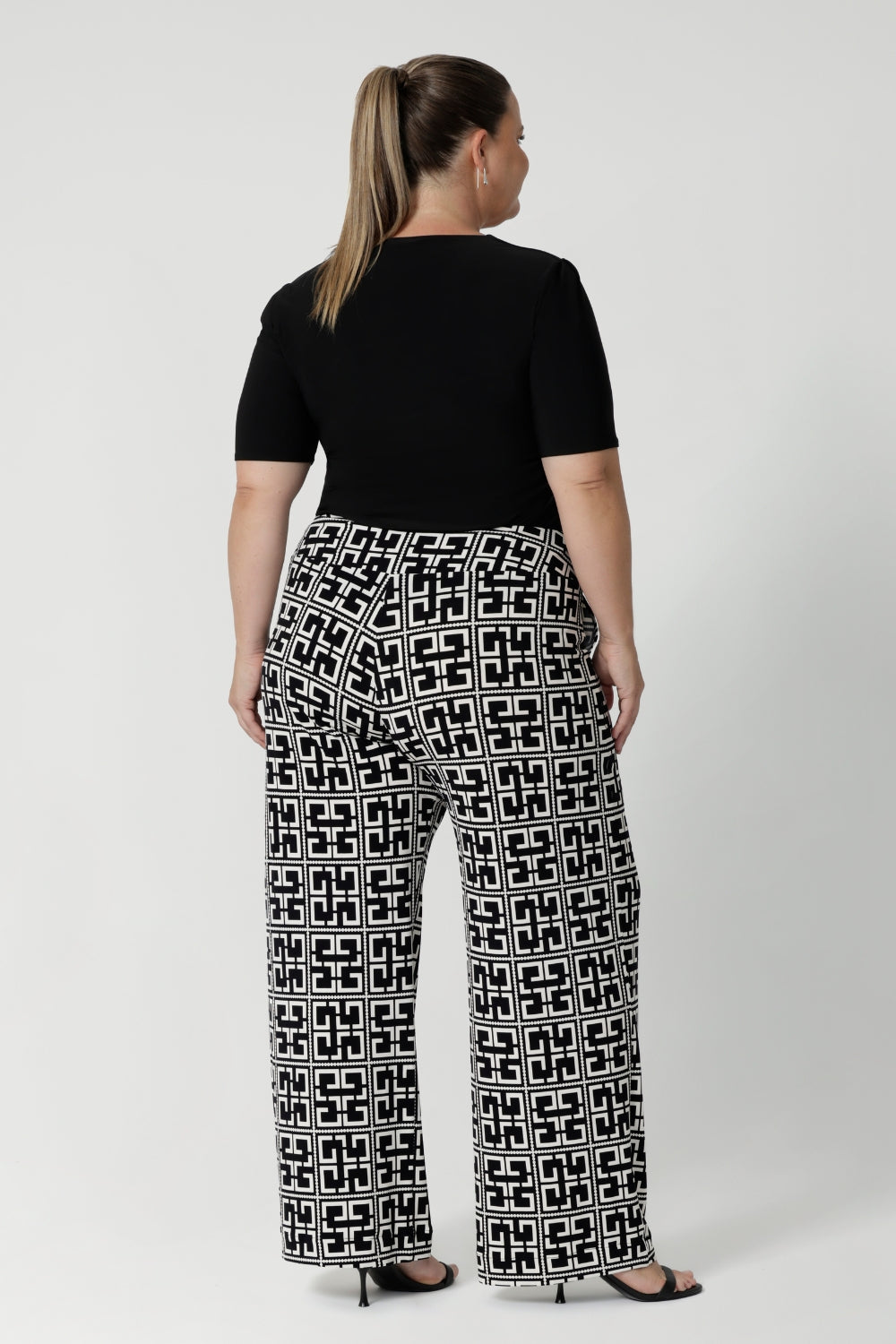 Back view image of size 18 woman wearing geometric printed workwear pants with black elbow length top and heels - curating an easy wear corporate look. Shop the Monroe Pant range in sizes 8-24.