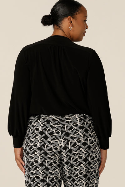 Back view of a plus size, size 18 woman wears a V-neck black top with long sleeves. This long sleeved top features cuffs at the wrists and a shirttail hemline. Made in Australia by Australian and New Zealand women's clothing label, L&F.