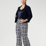 The Monroe Pant features a pull-on waistband that sits smoothly on the body, deep side pockets with topstitching for a tailored touch, and a classic straight-leg cut that transitions seamlessly from workwear to weekend. Size 10 woman wears petite height friendly pants with satin cami and navy jacket.