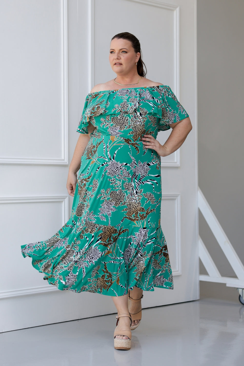  Plus sized woman wears the Myla dress in Jade Safari off the shoulders - a jade coloured dress with abstract animal print design. Maxi dress features side pockets and frill hem. Made in Australia and size inclusive for women size 8-24. 