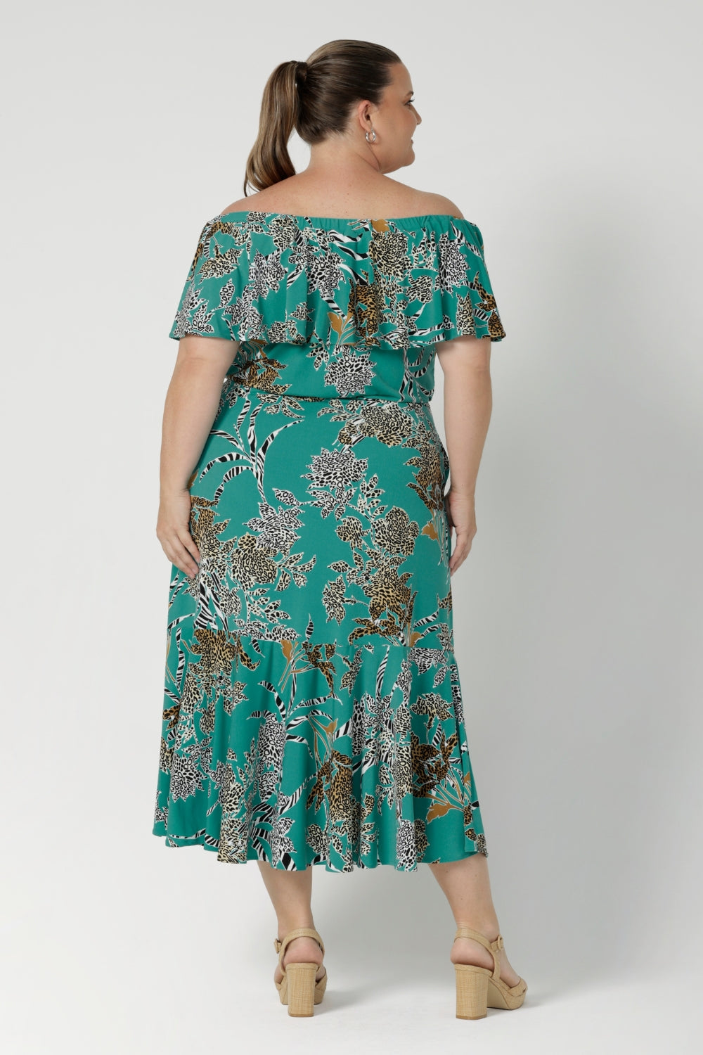 Back view of a woman wearing the Myla dress in Jade Safari off shoulder frill neck style. Side pockets and frill hem. Made in Australia and size inclusive for women size 8-24. 