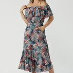 A woman wears the Myla dress in Whimsy an off shoulder frill neck style. Side pockets and frill hem. Made in Australia and size inclusive for women size 8-24. 