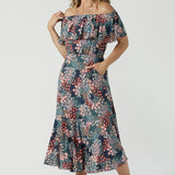 A woman wears the Myla dress in Whimsy an off shoulder frill neck style. Side pockets and frill hem. Made in Australia and size inclusive for women size 8-24. 