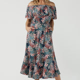 Worn on one shoulder. A woman wears the Myla dress in Whimsy an off shoulder frill neck style. Side pockets and frill hem. Made in Australia and size inclusive for women size 8-24. 