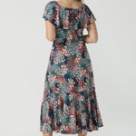Back view of a woman wearing the Myla dress in Whimsy an off shoulder frill neck style. Side pockets and frill hem. Made in Australia and size inclusive for women size 8-24. 