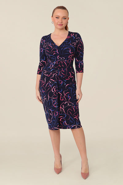 A women's workwear dress in pink and blue abstract print. This top features a V neckline and 3/4 sleeves with front ruffles. Shop this Australian-made top in petite to plus size women.