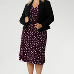 A classic V-neckline and full-length sleeves balance the design, making it perfect for cooler days or layered professional looks. Size 18 woman pairs a black tailored jacket over her spotted dress with black heels for a polished workwear look.