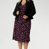 A classic V-neckline and full-length sleeves balance the design, making it perfect for cooler days or layered professional looks. Size 18 woman pairs a black tailored jacket over her spotted dress with black heels for a polished workwear look.